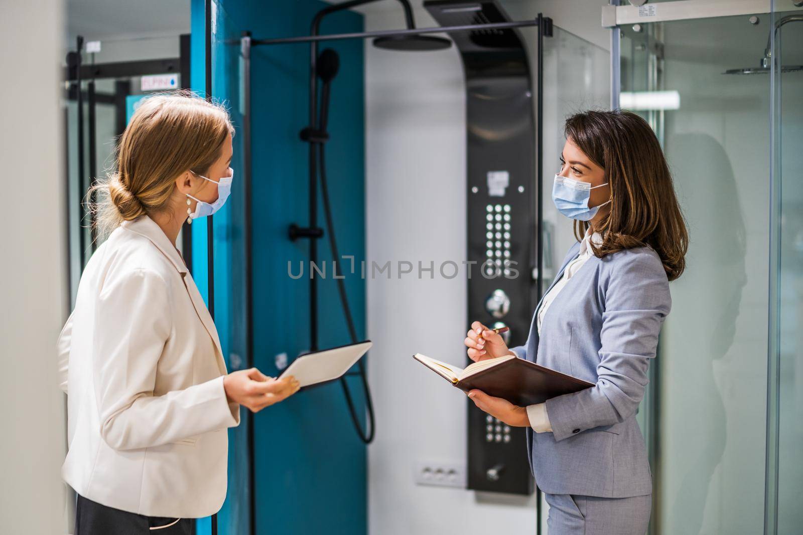 Businesswoman owning small business bath store. She is talking with a customer who is choosing the goods. They are wearing protective face mask.