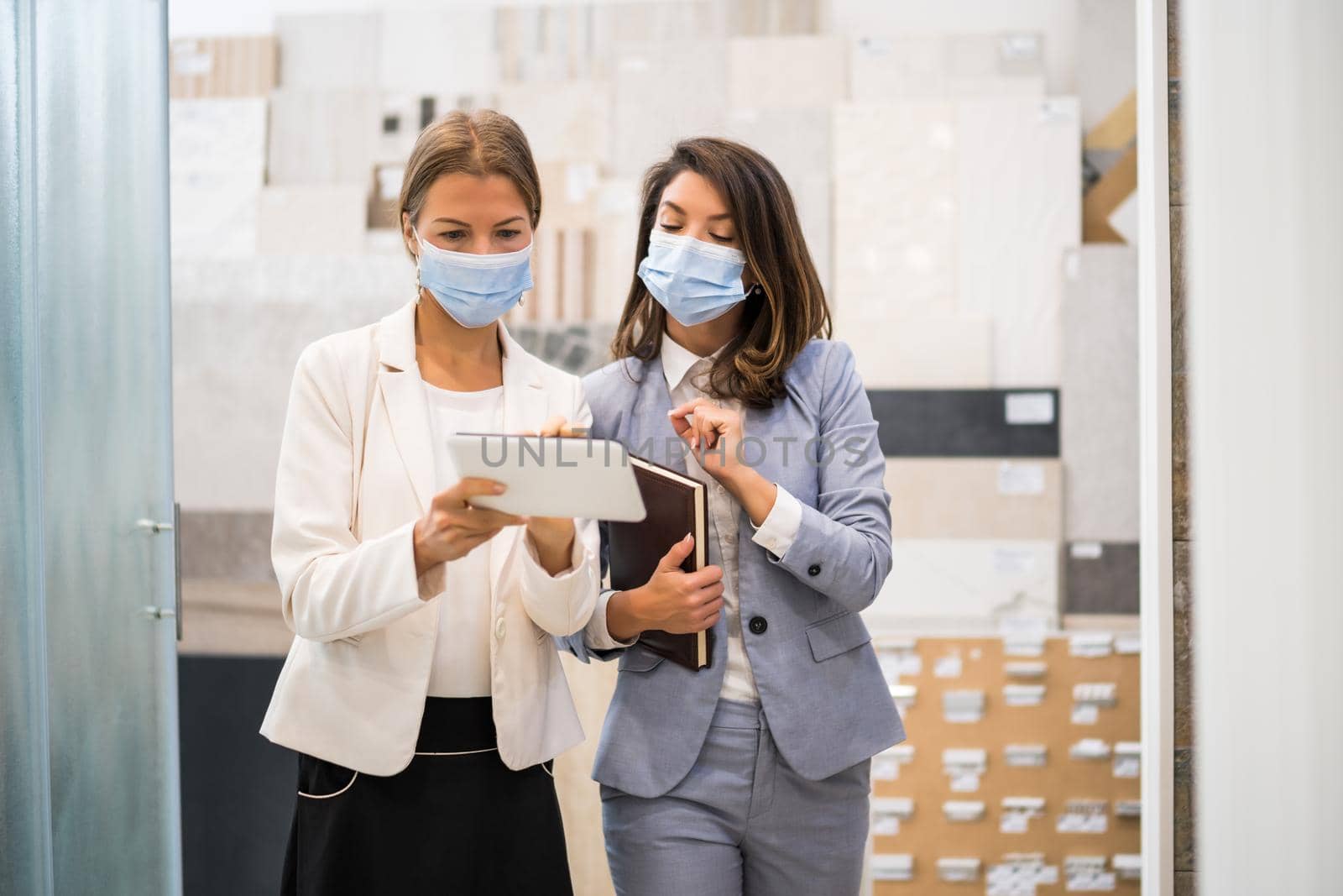 Businesswoman owning small business bath store. She is talking with a customer who is choosing the goods. They are wearing protective face mask.