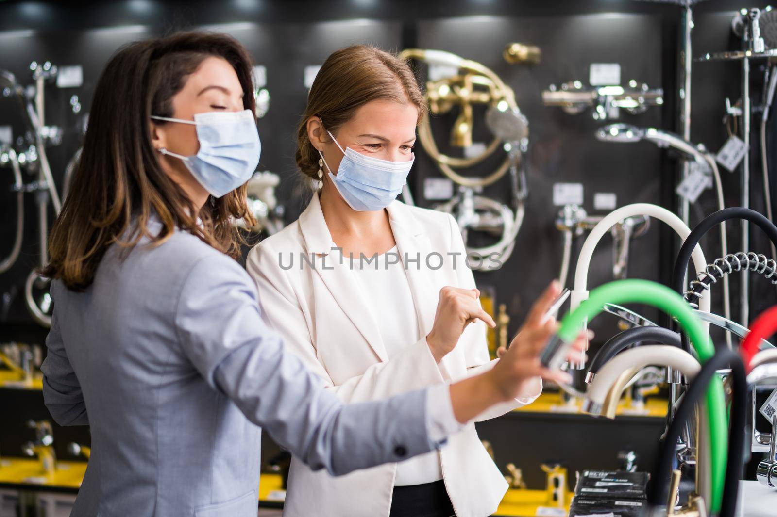 Businesswoman owning small business bath store. She is talking with a customer who is choosing the goods. They are wearing protective face mask.