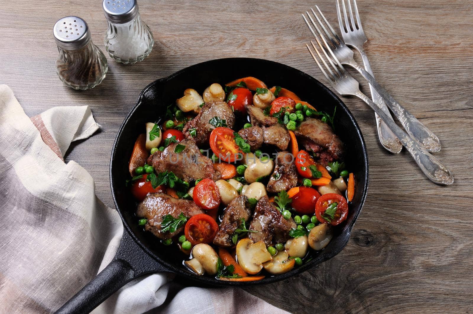 Fried chicken liver with vegetable side dish of tomatoes, carrots, mushrooms, peas in a pan