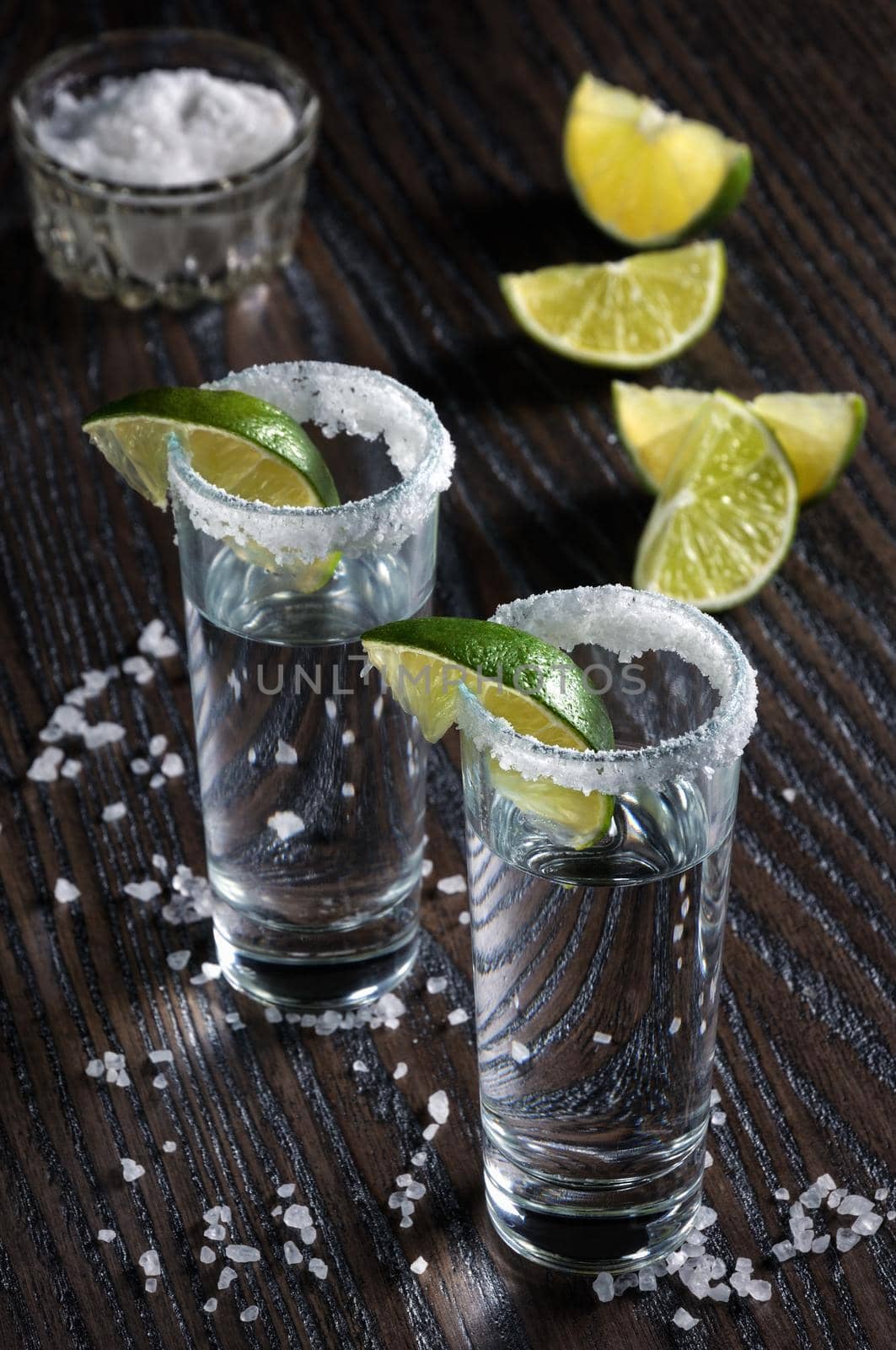 Portion of tequila, framed with a salt edge with slice lime in tall shot glasses