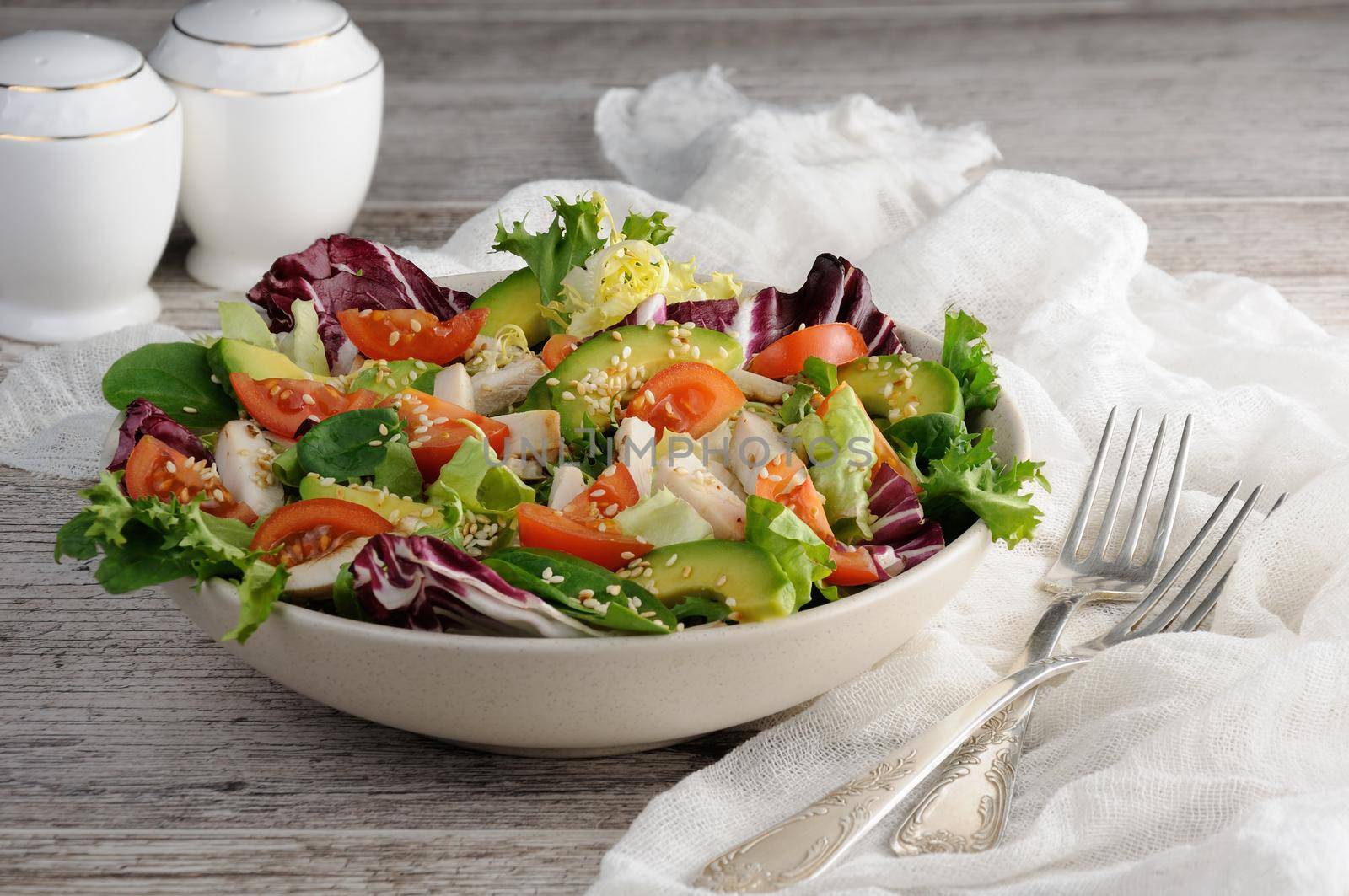 Light salad organic mix lettuce with tomatoes, avocado, slices of chicken breast, seasoned roasted sesame seeds.