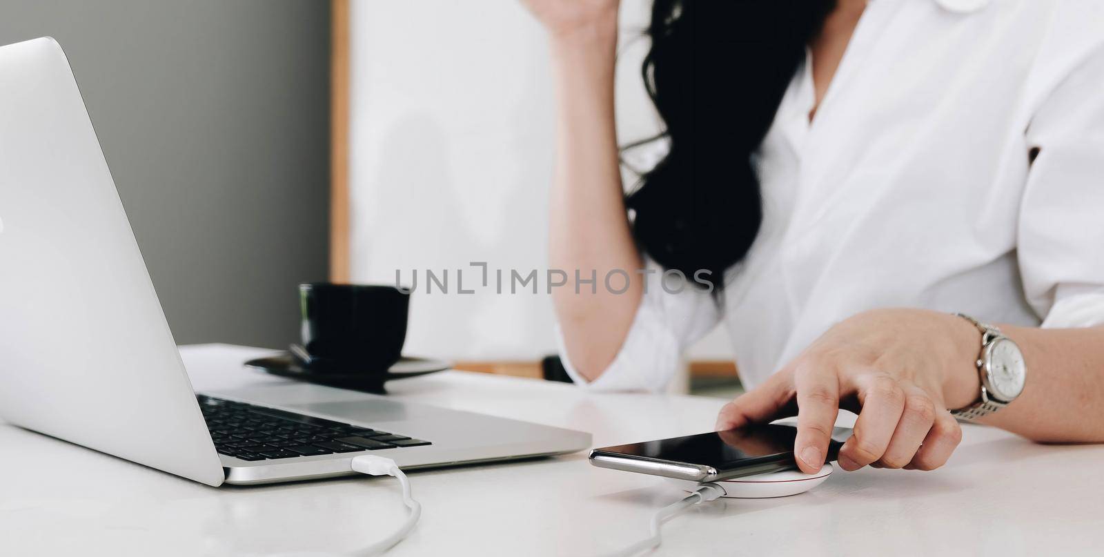 woman working at table while his mobile phone charging with wireless device by wichayada