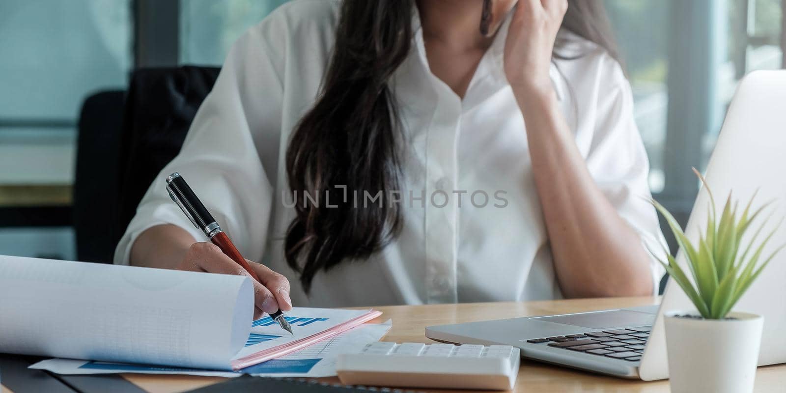 Close up of businesswoman or accountant hand holding pen working on laptop computer for calculate business data, accountancy document and calculator at office, business concept.