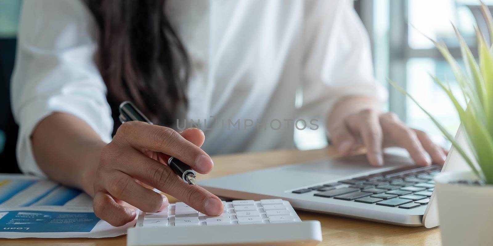 Close up Businesswoman using calculator and laptop for do math finance on wooden desk in office and business working background, tax, accounting, statistics and analytic research concept.