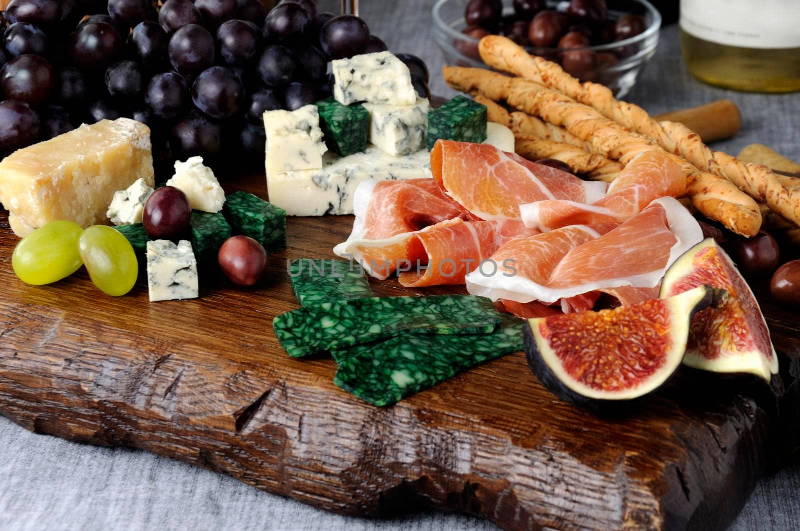 Dishes for Antipasto on a wooden board with prosciutto, different types of cheese, grapes and figs