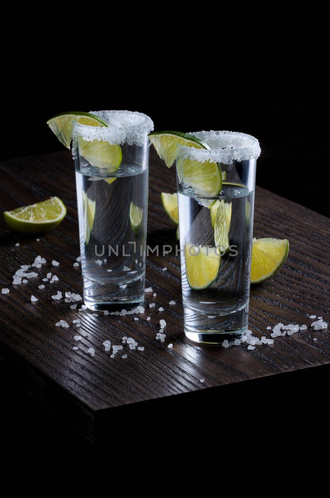 Portion of tequila, framed with a salt edge with slice lime in tall shot glasses
