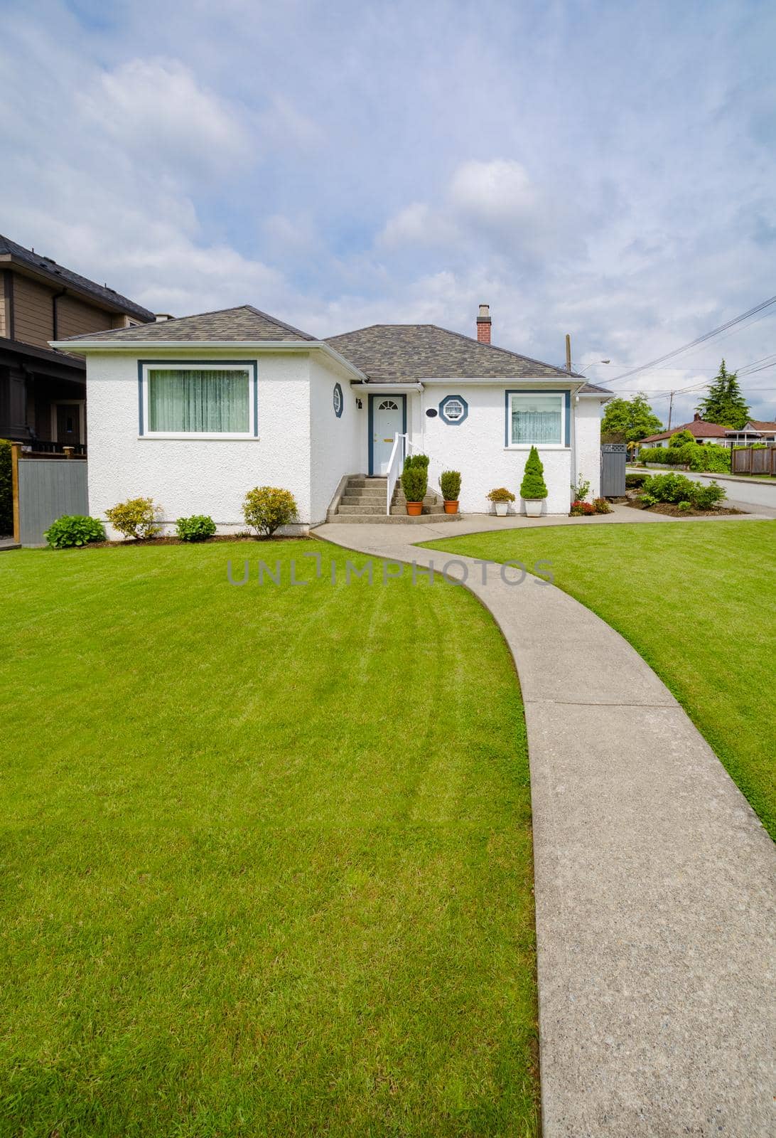 Main entrance of small residential house with concrete walkway over green lawn of front yard. Family house with doorsteps to the entrance