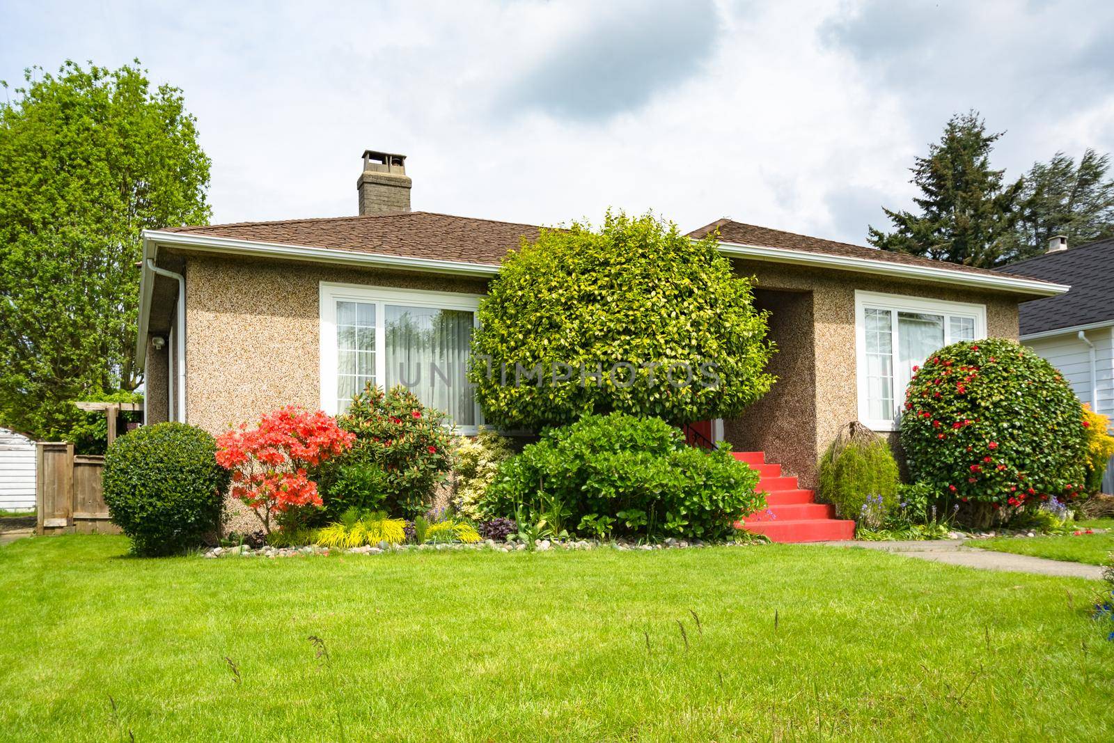 Modest residential house with concrete pathway over green lawn of the front yard on cloudy day