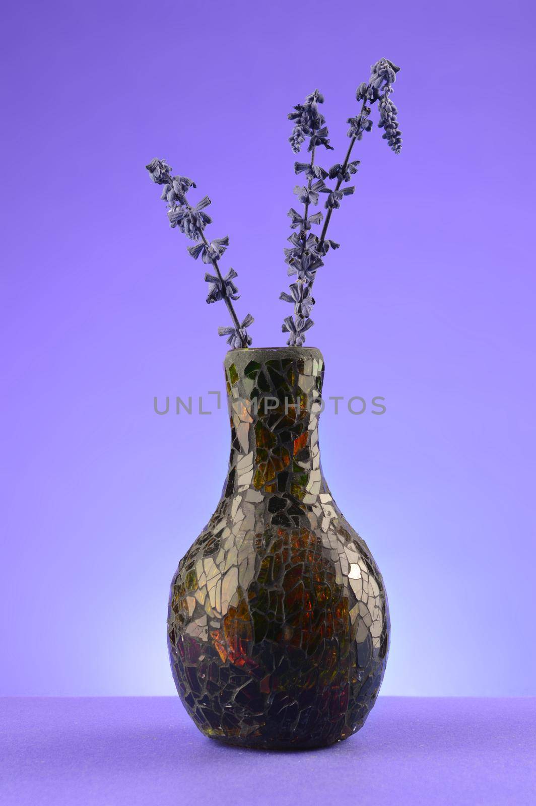 A decorative vase with some freshly dried lavender over a monochromatic violet colored background.
