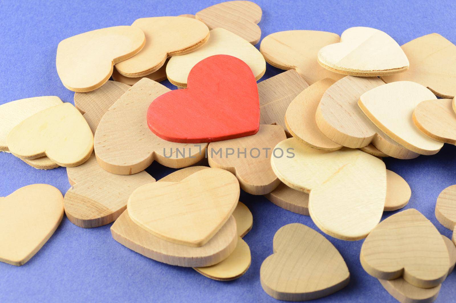 A red wood heart is singled out over top all the other uncolored wood shaped hearts.