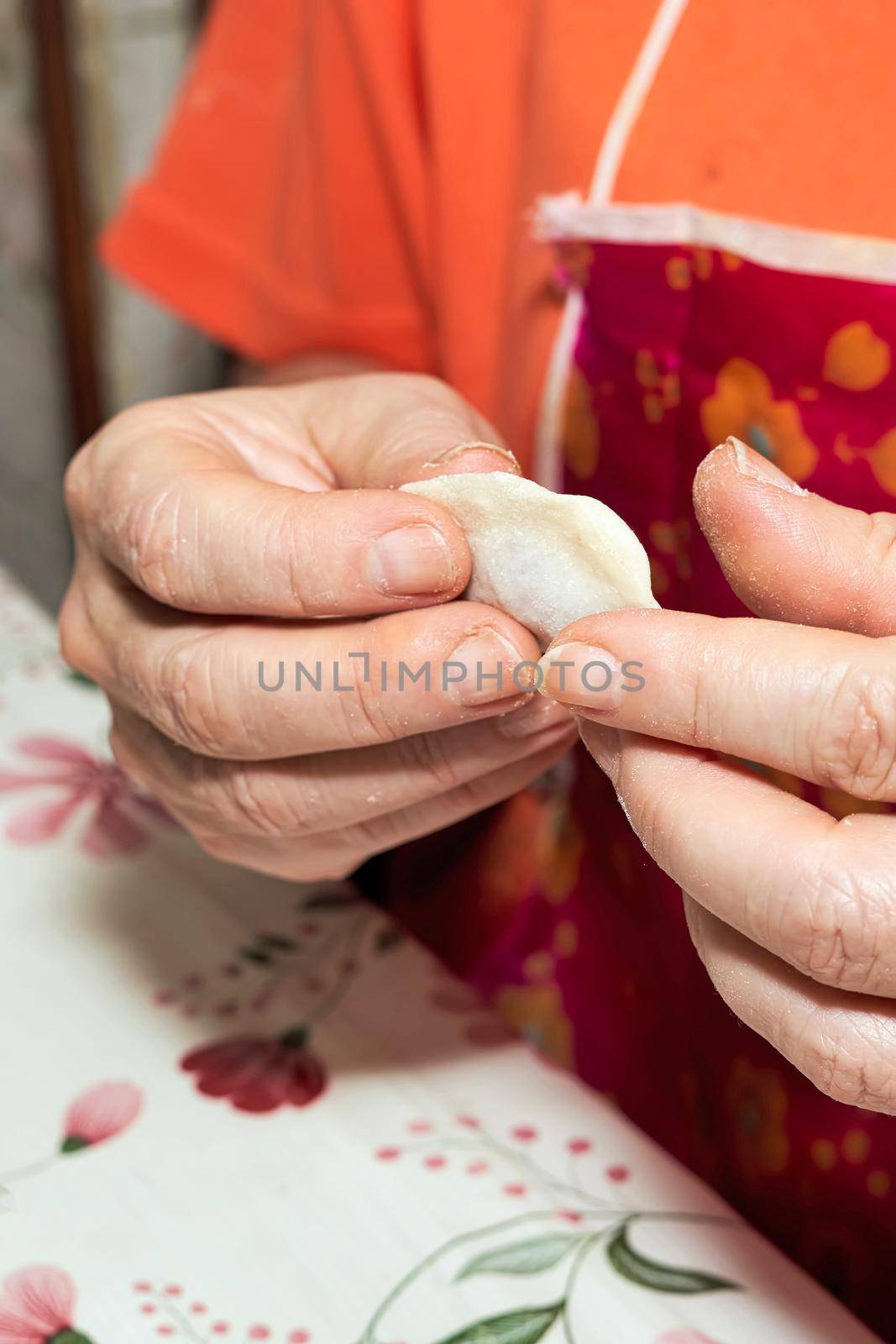 Hands soiled with flour hold a raw dumpling. Cooking homemade dumplings. Vertical shot