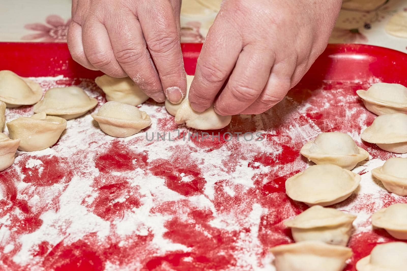 A hand is placing raw dumplings on a red floured tray. Cooking at home