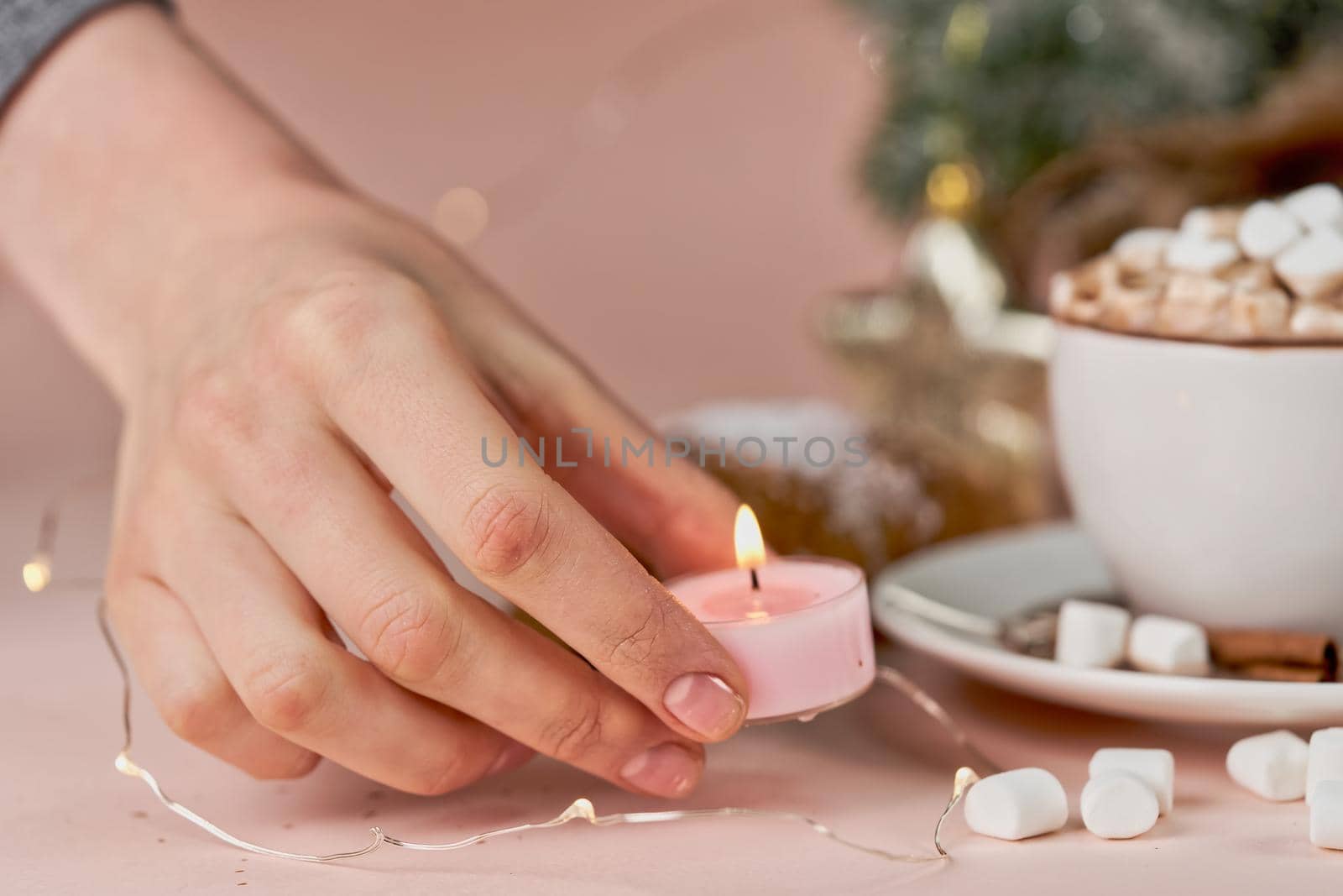 A hand puts a lit candle on the table next to a mug with coffee and marshmallows by vizland