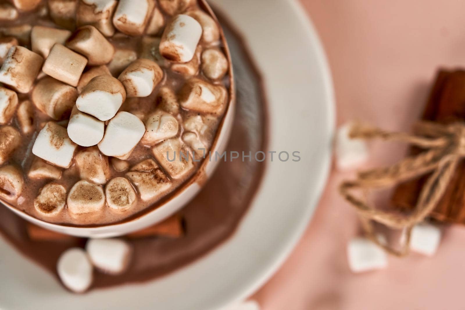 A white mug and saucer poured coffee with marshmallows and cinnamon tied with a rope. Top view close up