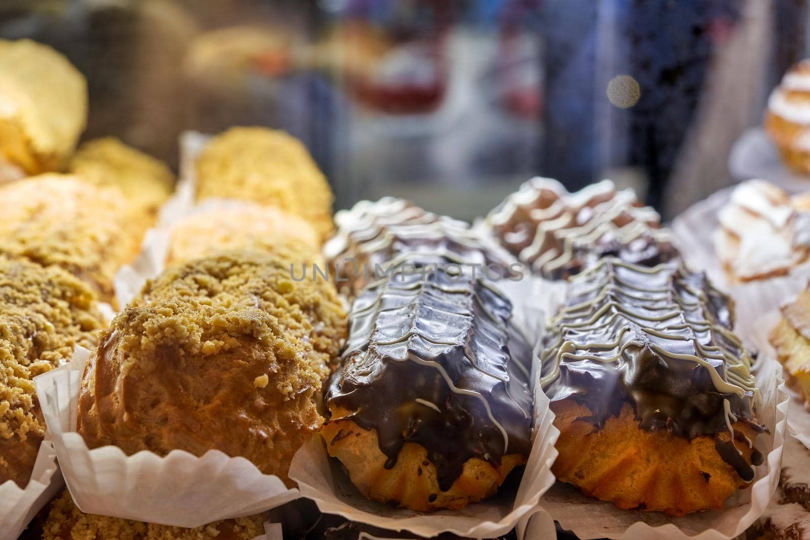 Fragment of a bakery showcase, close up. Eclair cakes of different types on paper stands