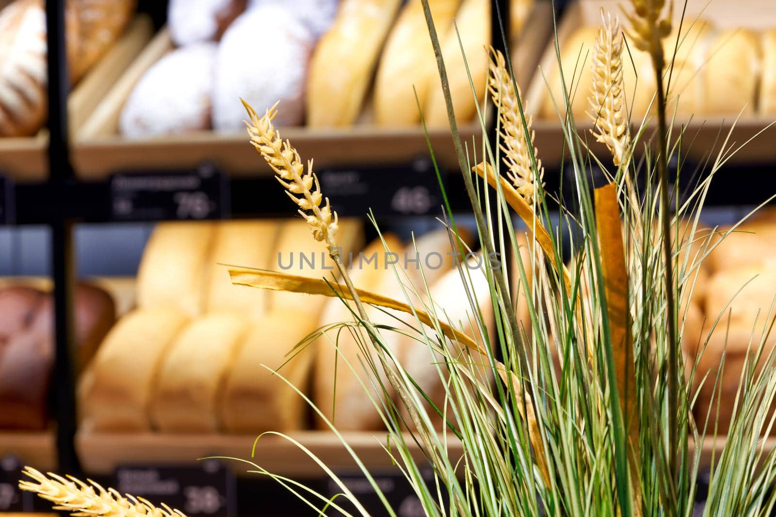 Spikelets of wheat on the background of shelves with bread in a bakery by vizland