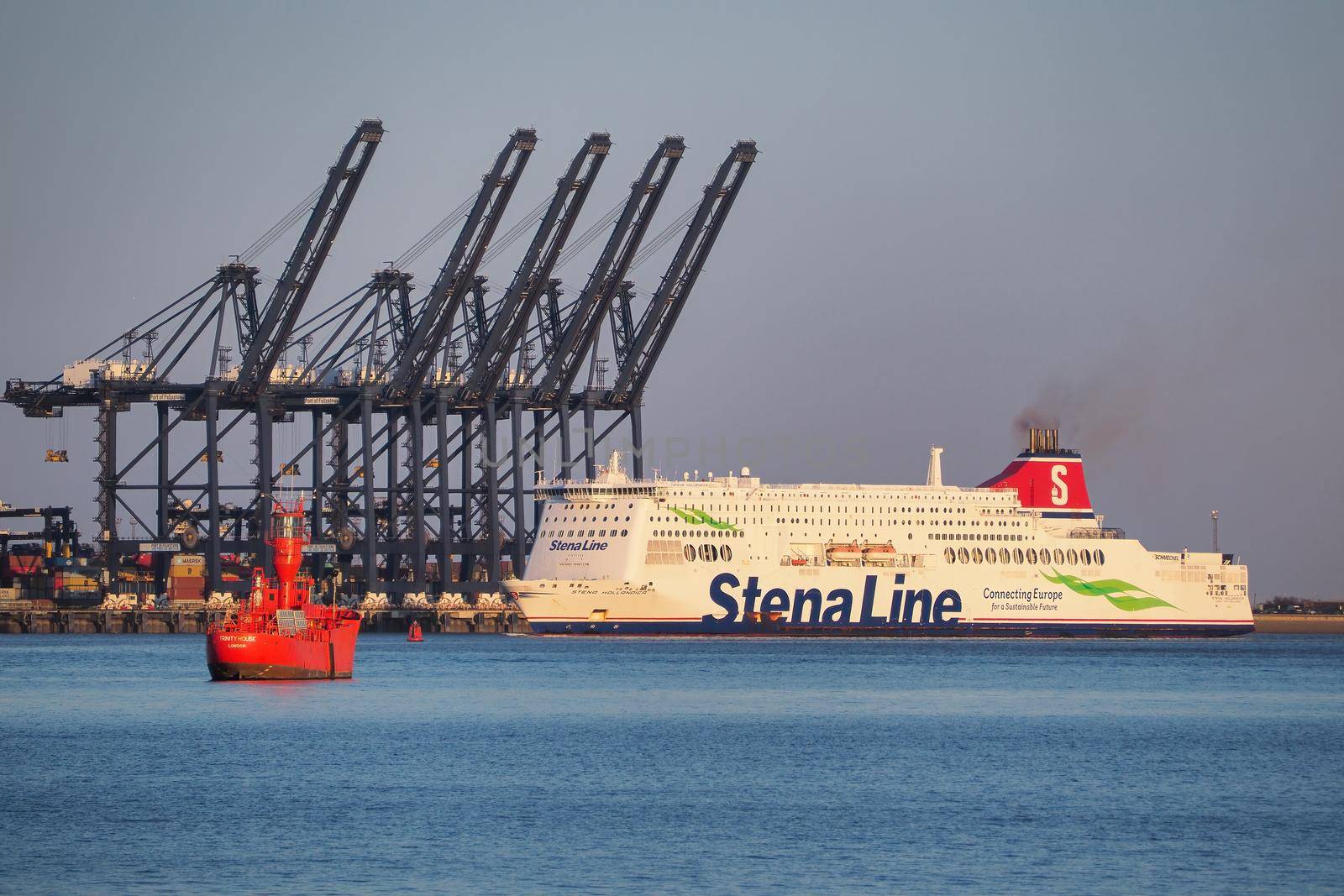 Shotley Point, Suffolk, UK, April 12 2021: Stena Line ferry Stena Hollandica steaming past the Port of Felixstowe dock cranes and red lightship at dusk