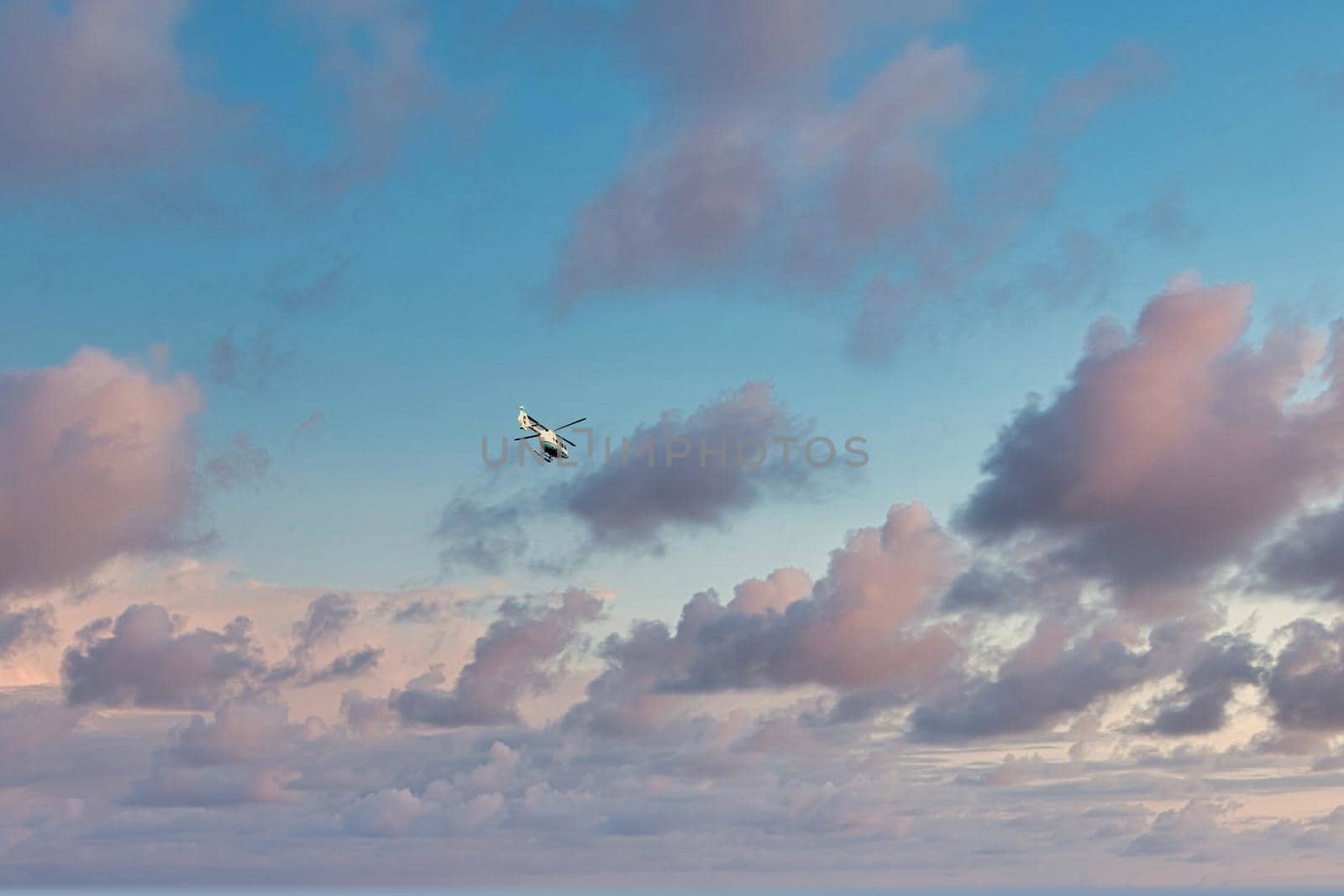 The helicopter flies against the background of the evening cloudy sky during the sunset