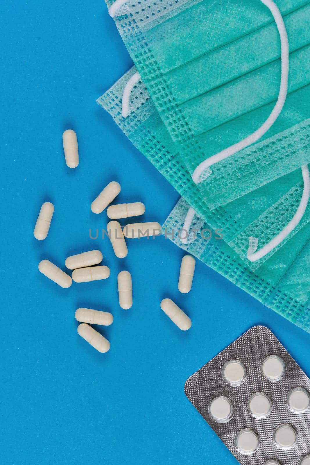 Medical masks, white capsules and pills in packaging on a blue background. Top view, vertical shot