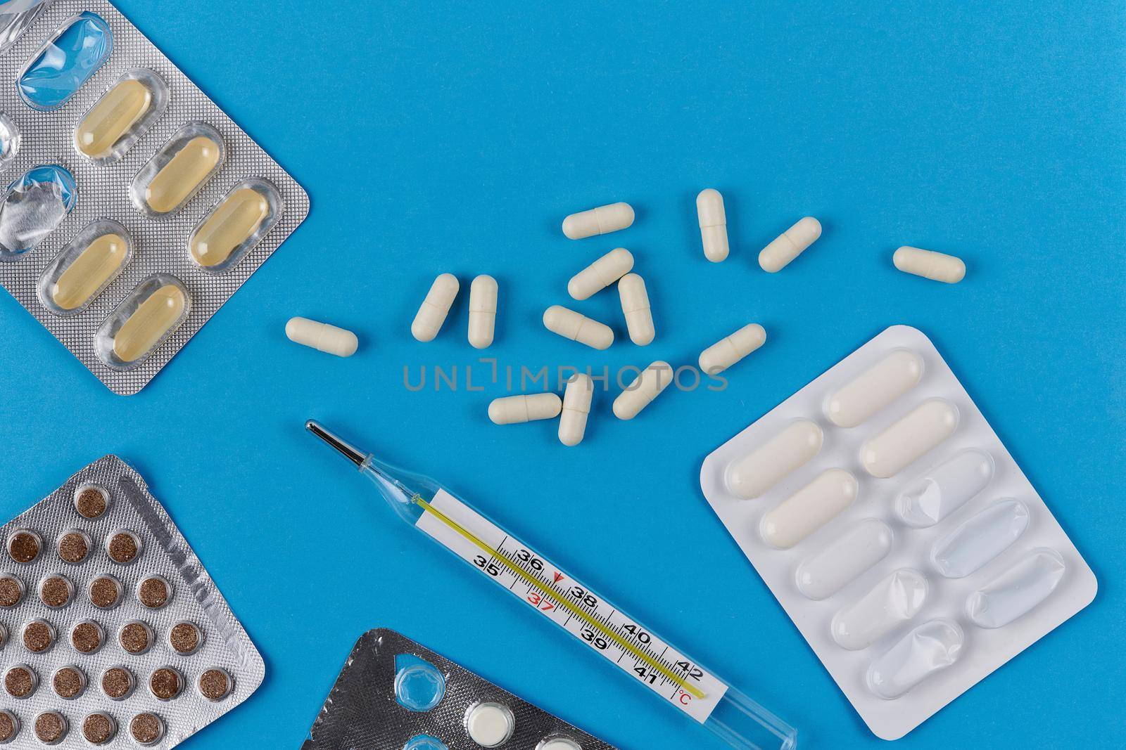 Mercury glass thermometer, white capsules and tablets in packaging on a blue background. View from above