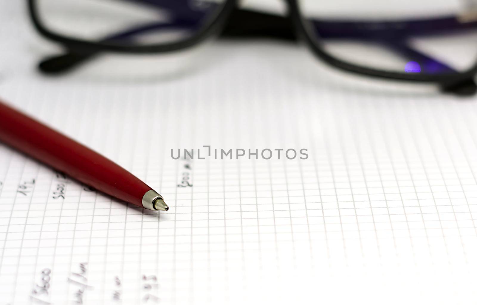 Red ballpoint pen on the white pages of an open notebook with a pair of eyeglasses in the background. Inspiration and storytelling.