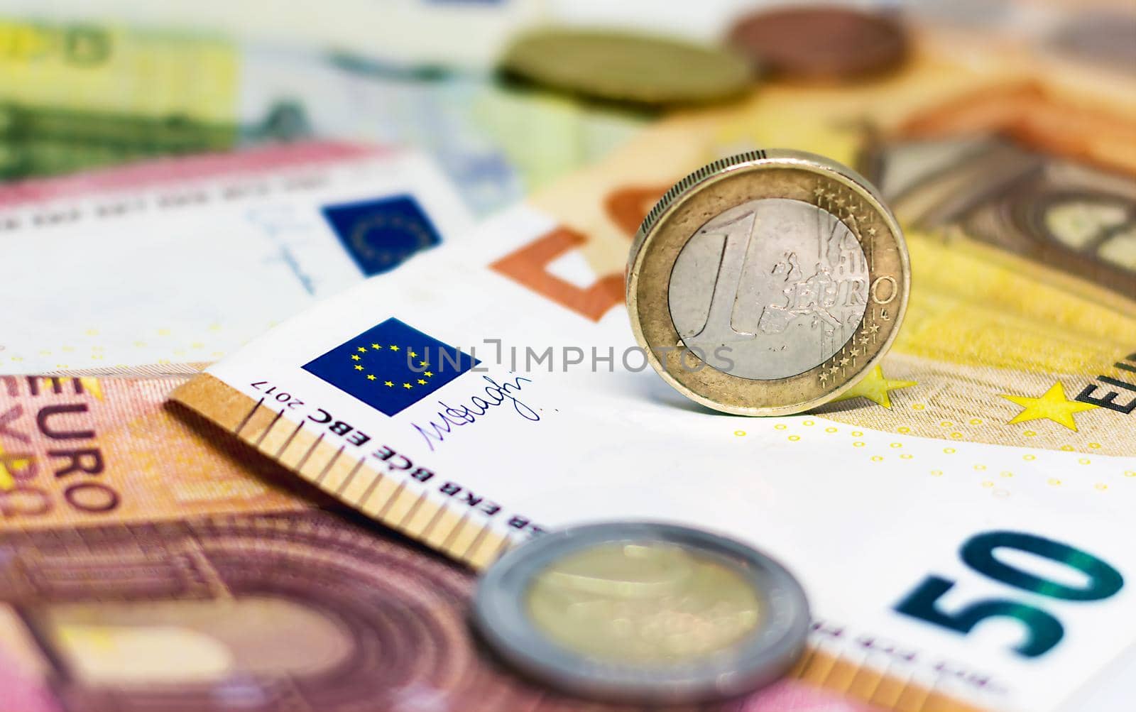A used 1 euro coin standing on top of some euro banknotes by rarrarorro
