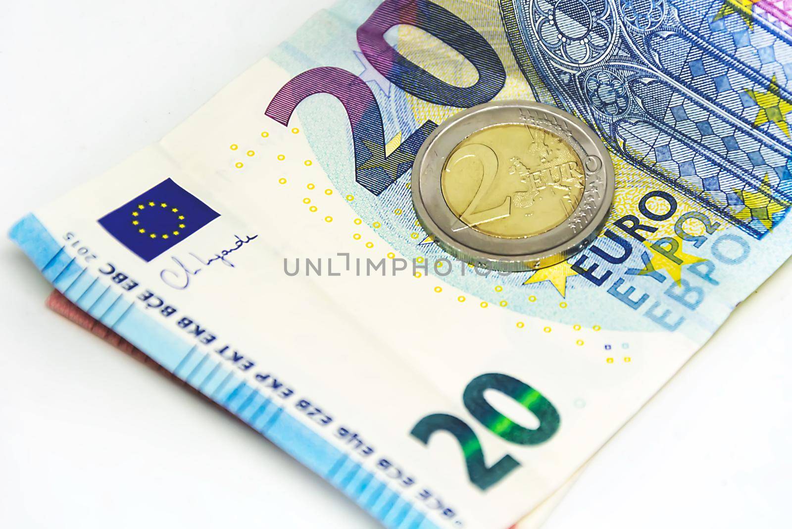 A used 2 euro coin standing on top of a 20 euro banknote. Economics and finance in the European Union.