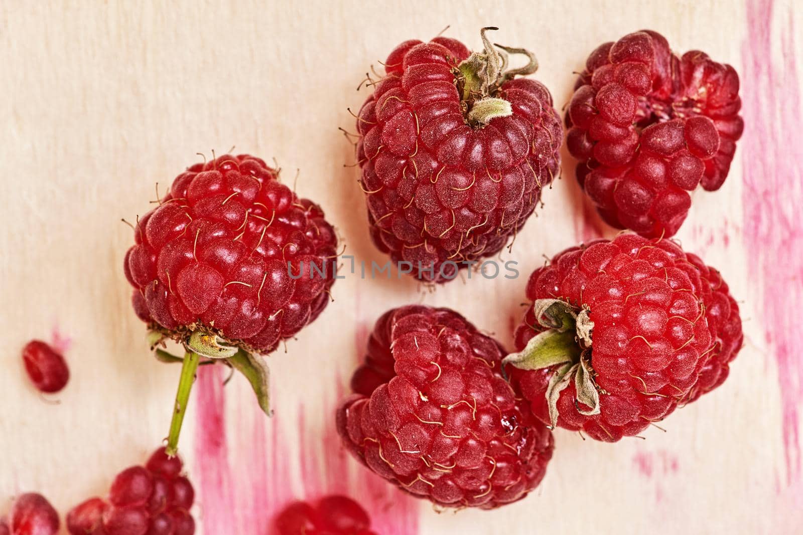 A fragment of a wooden container with ripe red raspberries and with juice stains from berries. Top view close up