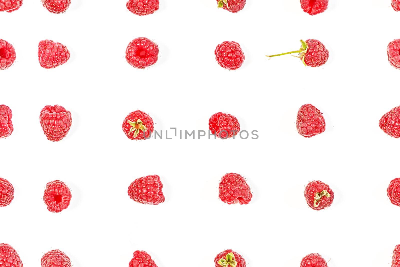 A pattern of ripe red raspberries laid out in lines on a white background in various poses. View from above
