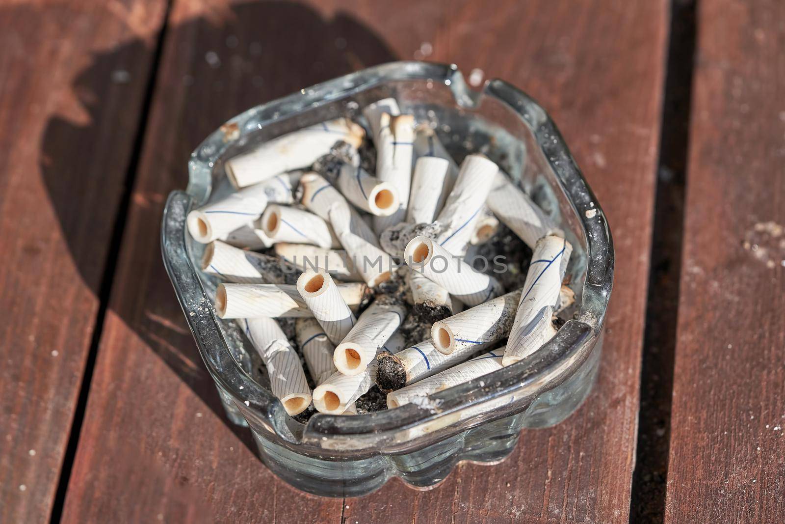 There are many cigarette butts in the ashtray. Top view of brown planks background