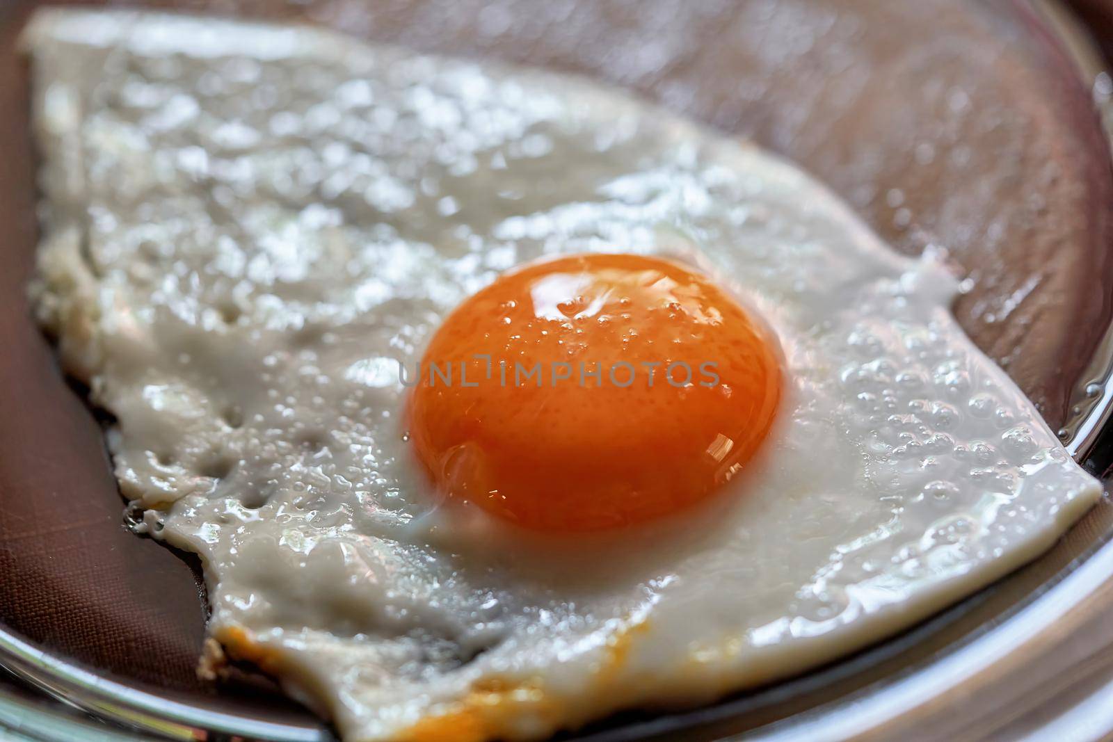 Fried egg with a whole round yolk on a transparent glass plate. Tasty breakfast