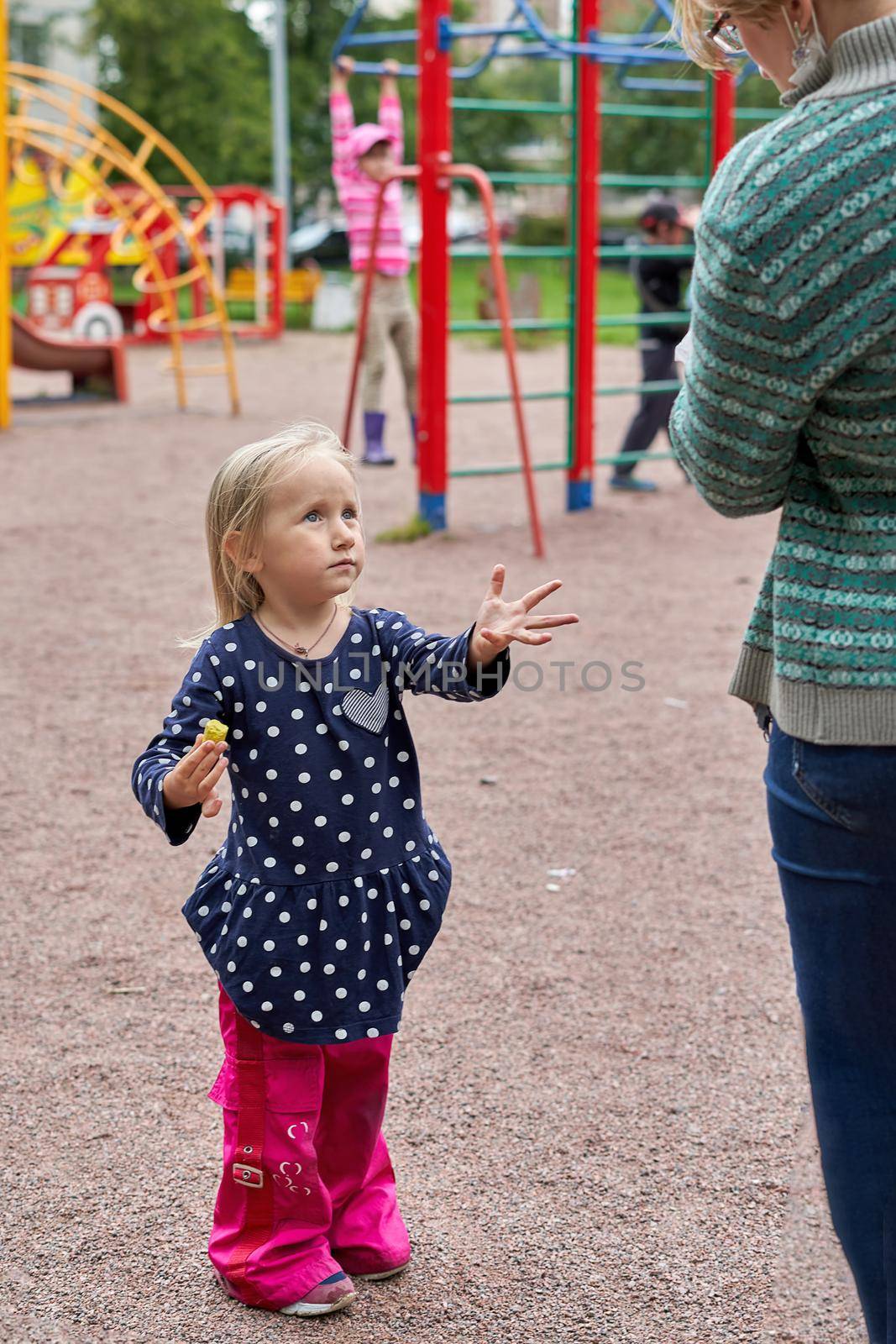Little girl pulls her hand to her mother for food on the background of a children's playground