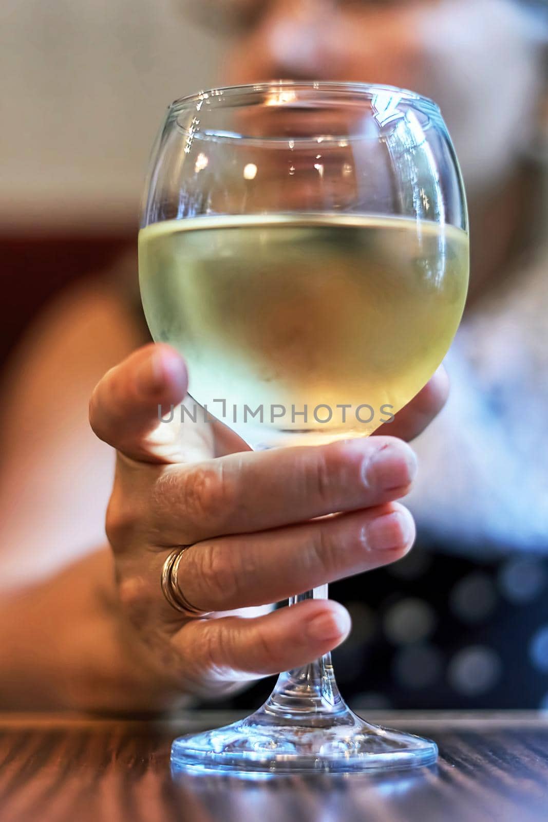 Woman's hand holding a glass of white wine on a blurred face background