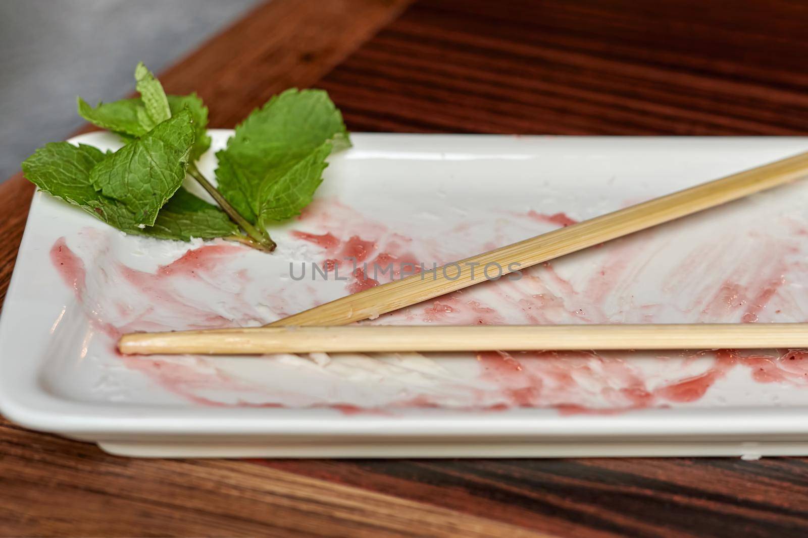 Empty white rectangular plate with wooden chopsticks. Leftover jam and mint leaves