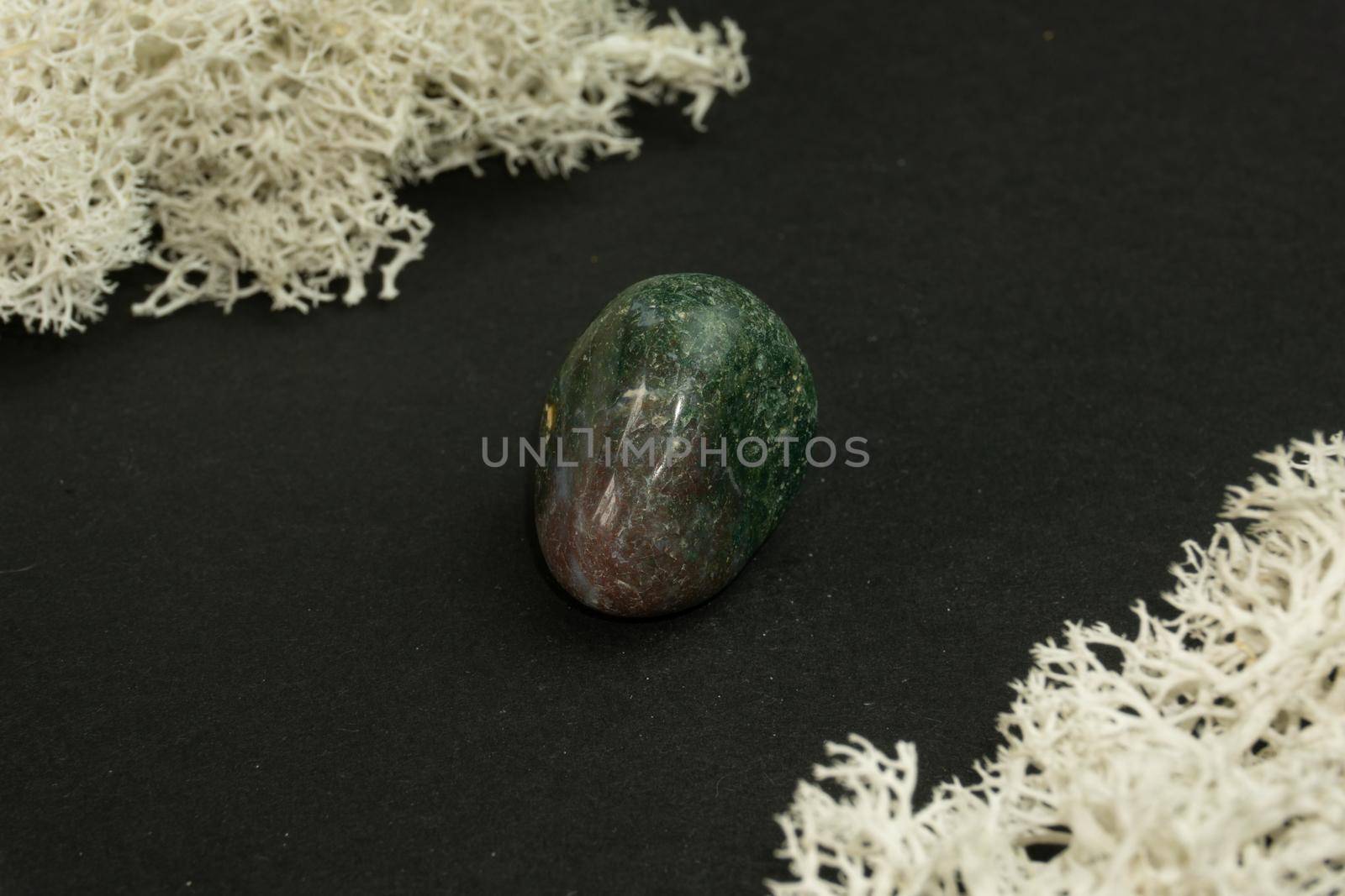 Heliotrope from India. Natural mineral stone on a black background surrounded by moss. Mineralogy, geology, magic, semi-precious stones and samples of minerals. Close-up macro photo.