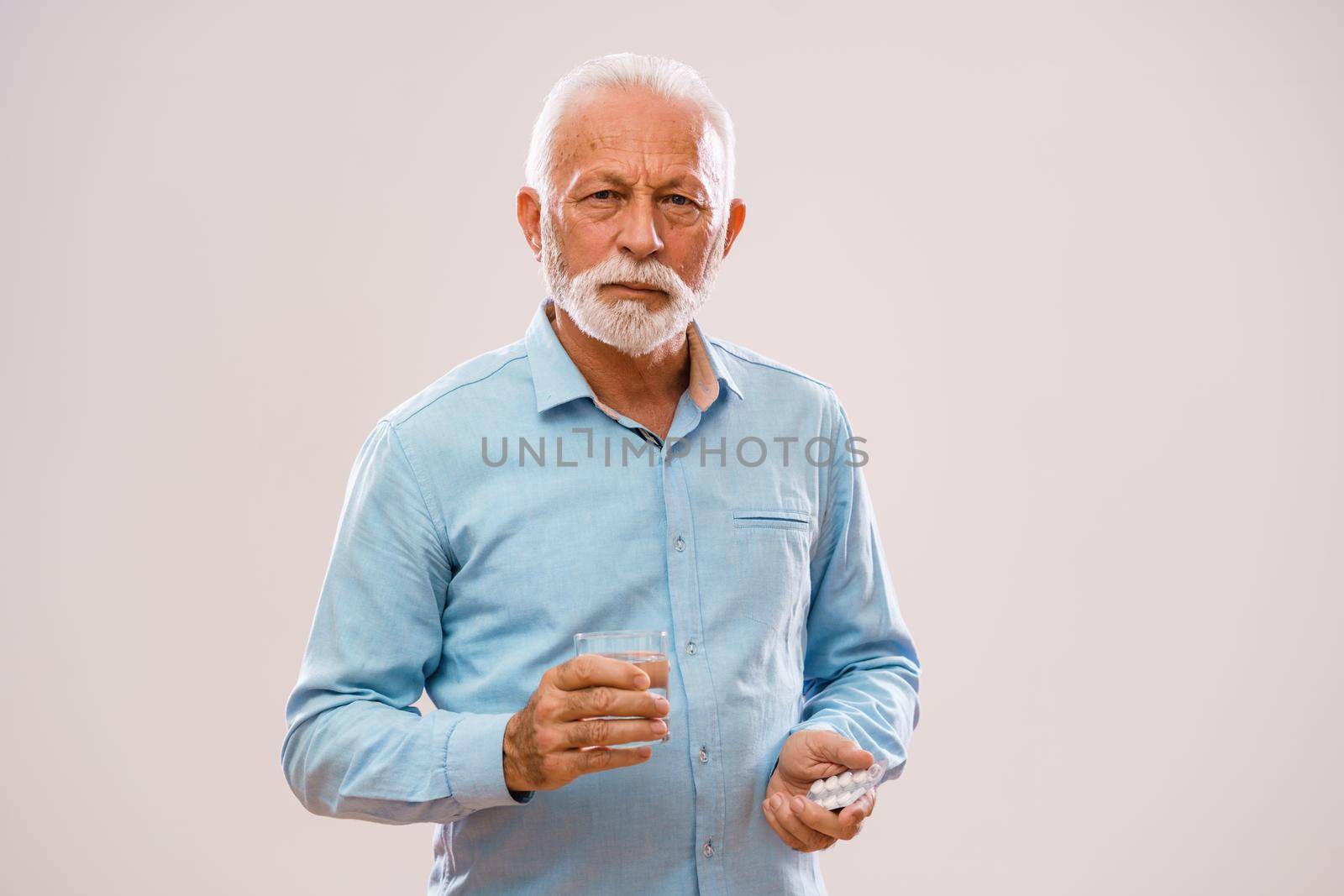 Portrait of serious senior man who is holding medicine and glass of water.