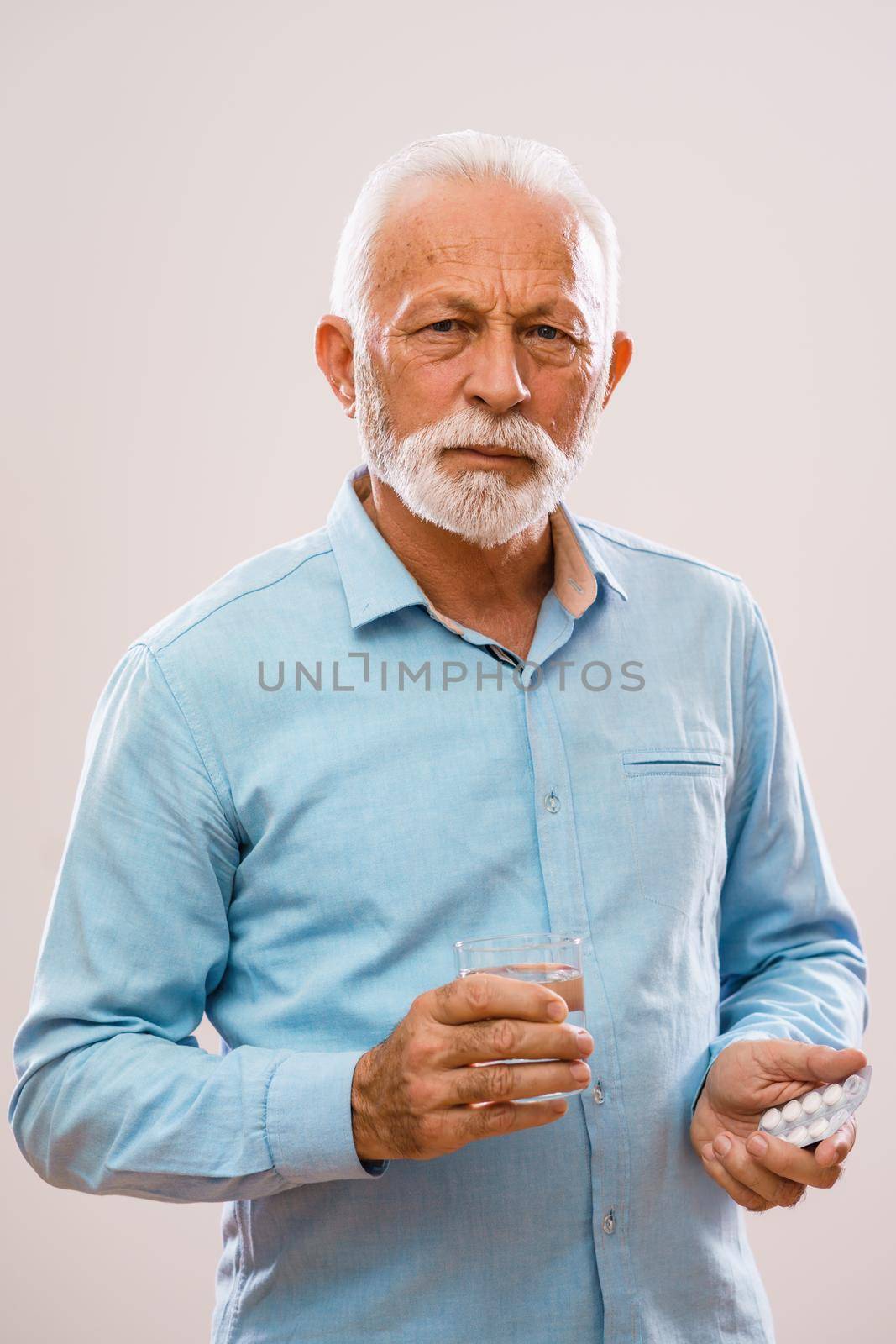 Portrait of serious senior man who is holding medicine and glass of water.