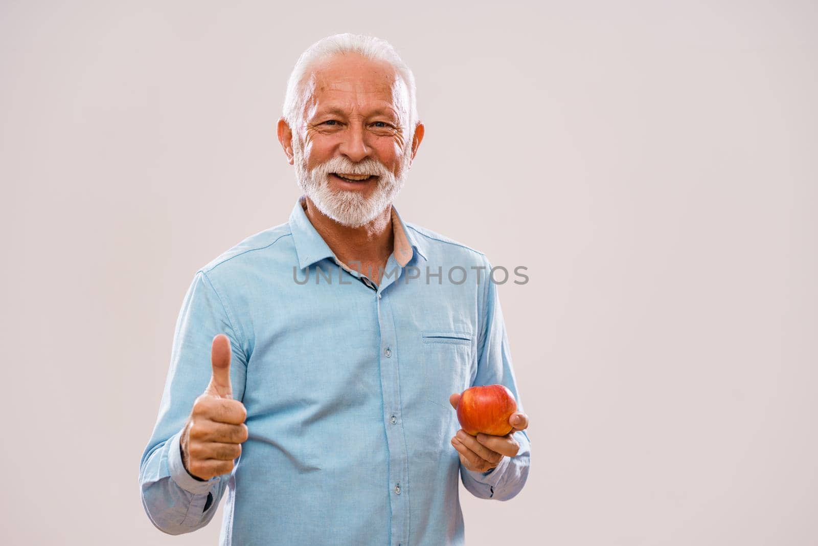 Portrait of cheerful senior man who is holding apple and smiling.
