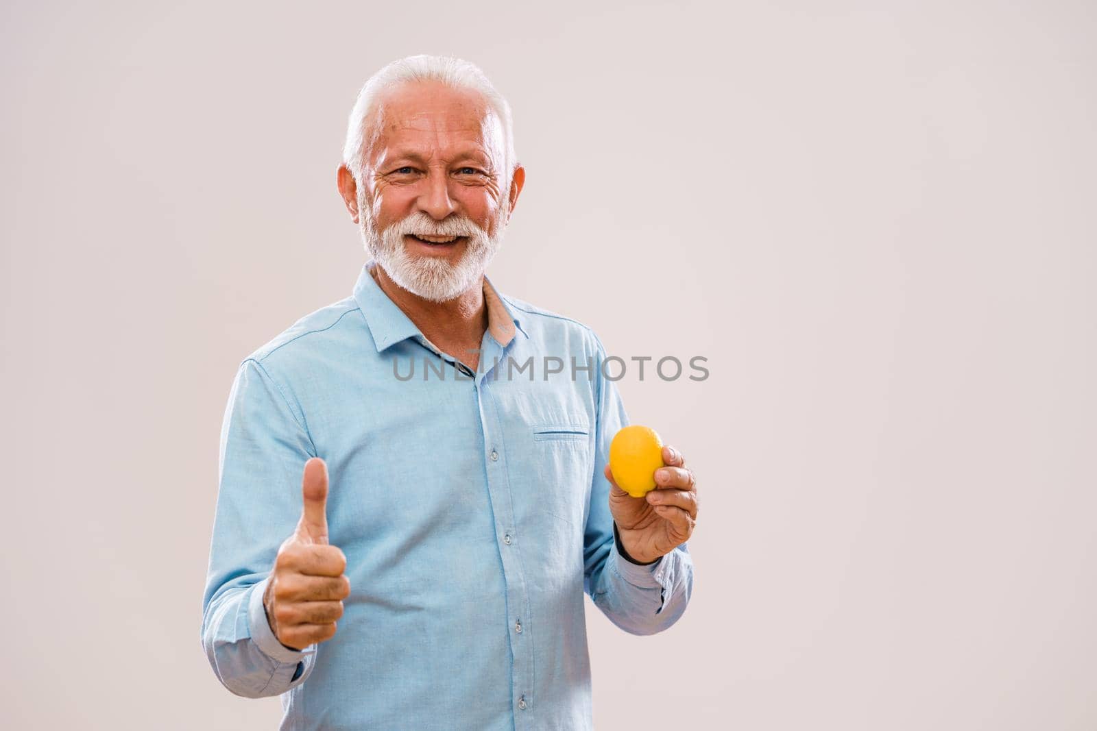 Portrait of cheerful senior man who is holding lemon and smiling.