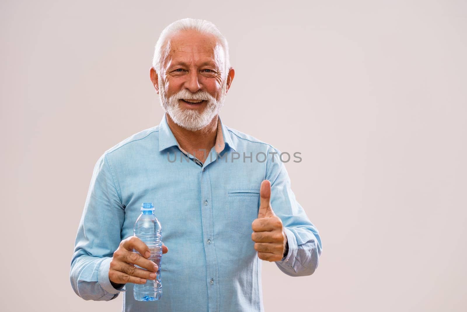 Portrait of cheerful senior man who is holding bottle of water and smiling.