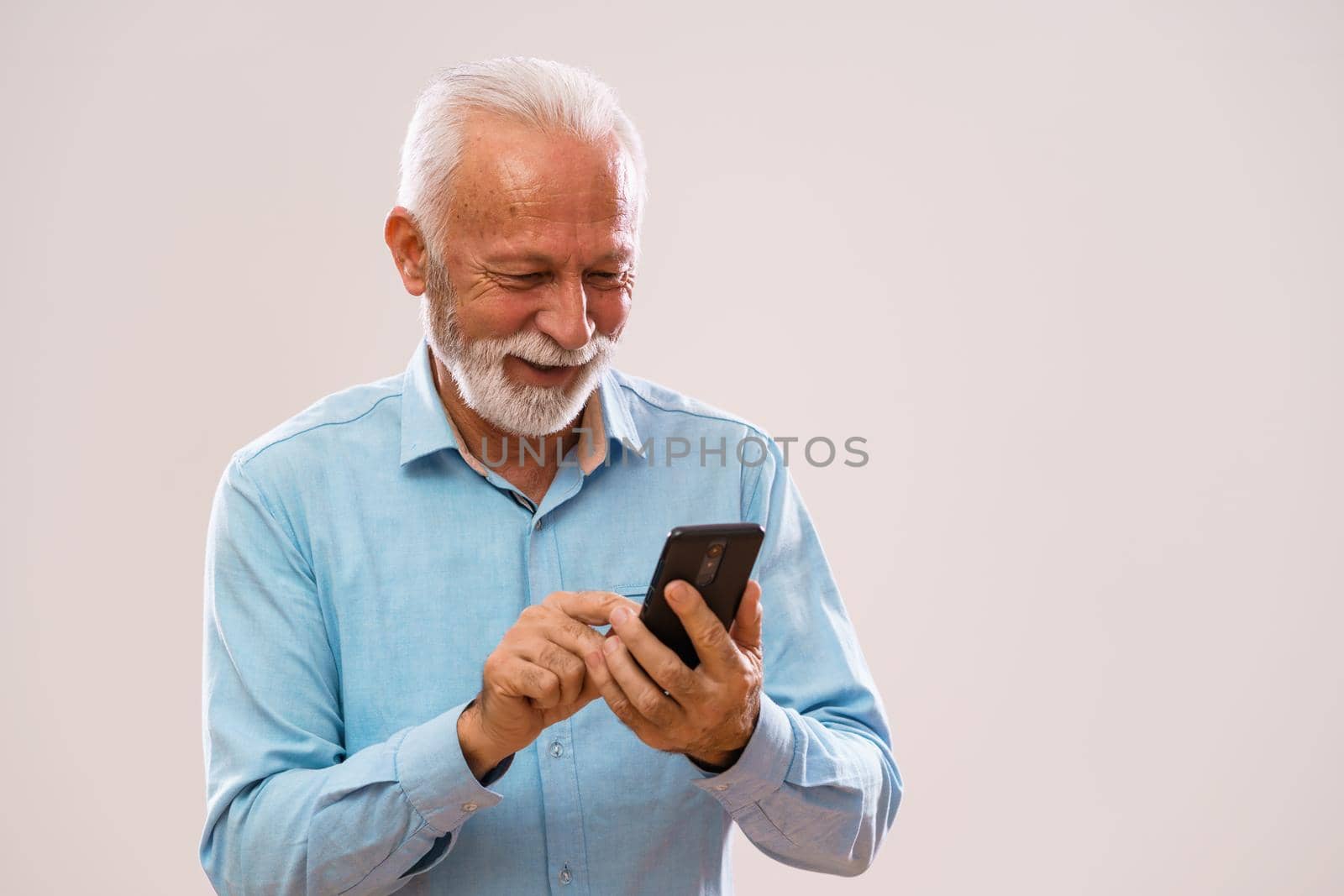 Portrait of cheerful senior man who is using smartphone.