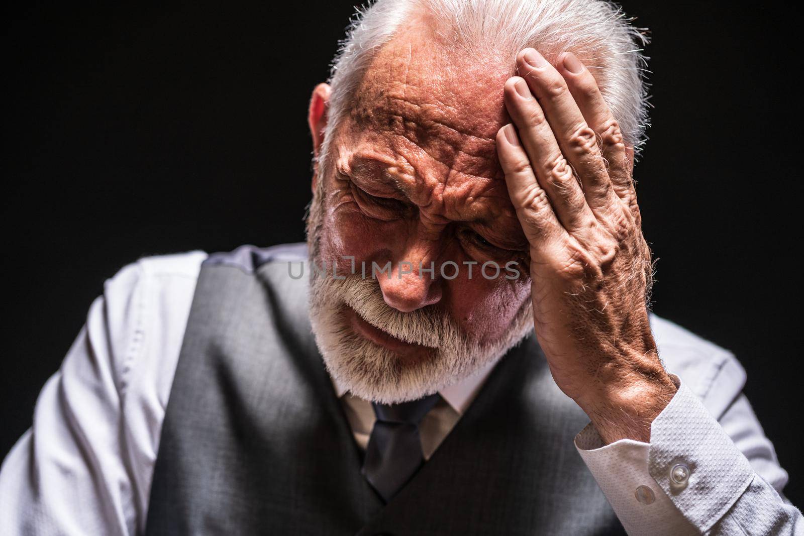 Portrait of depressed senior man on black background.