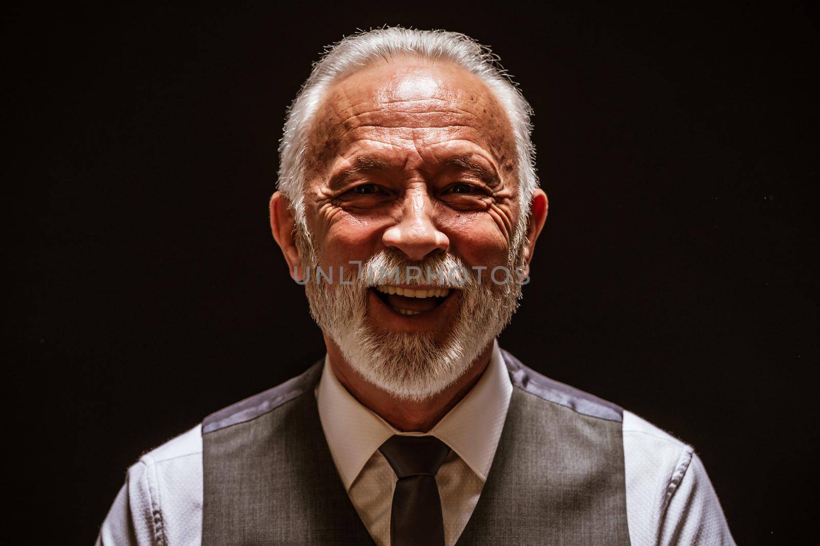 Portrait of cheerful senior man on black background.