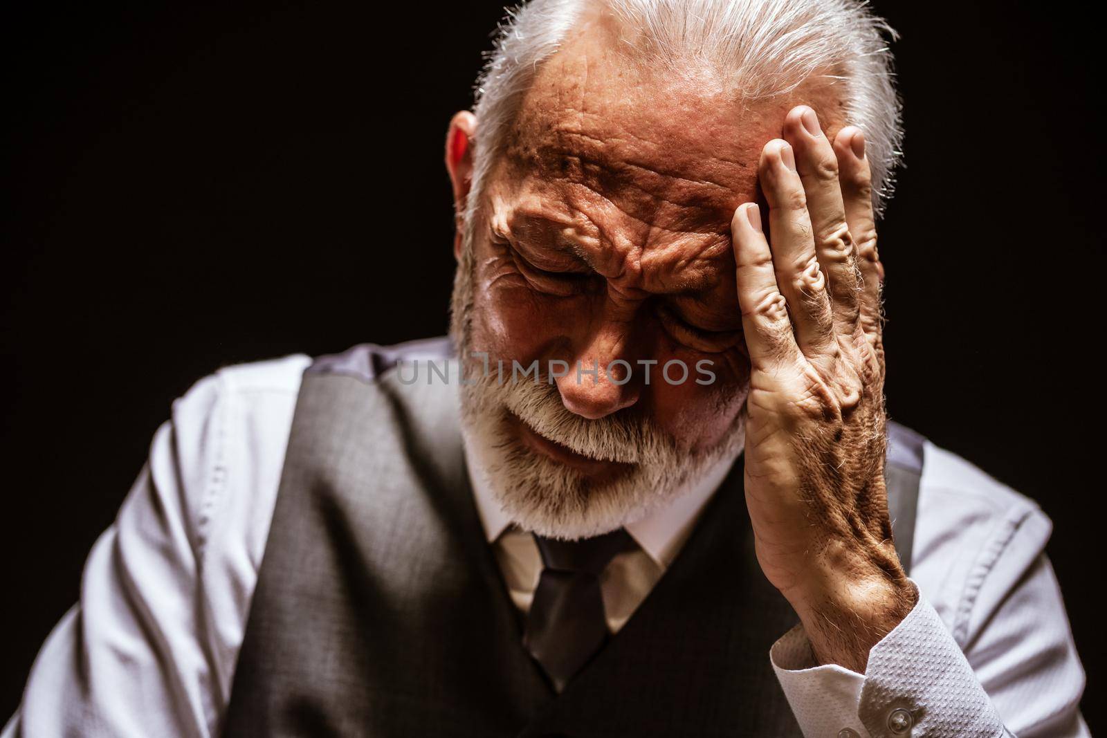Portrait of depressed senior man on black background.