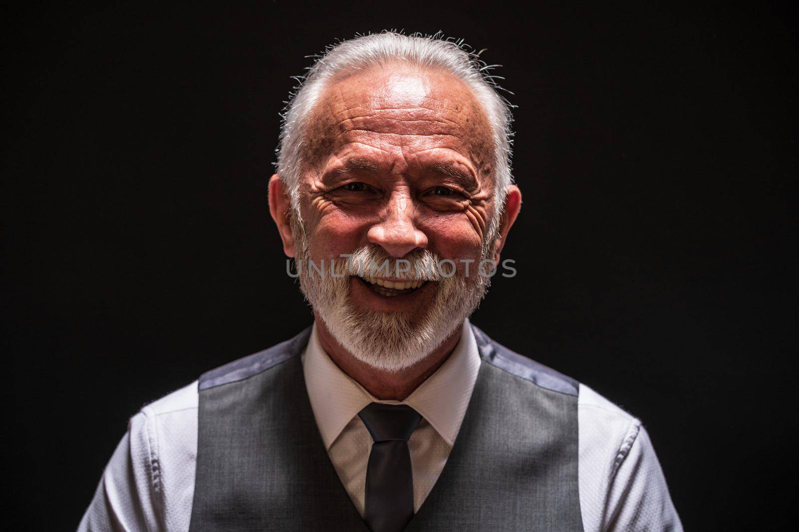 Portrait of cheerful senior man on black background.