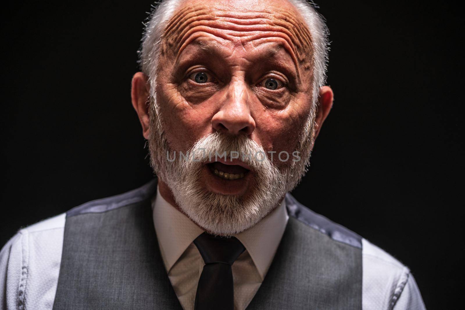 Portrait of surprised senior man on black background.