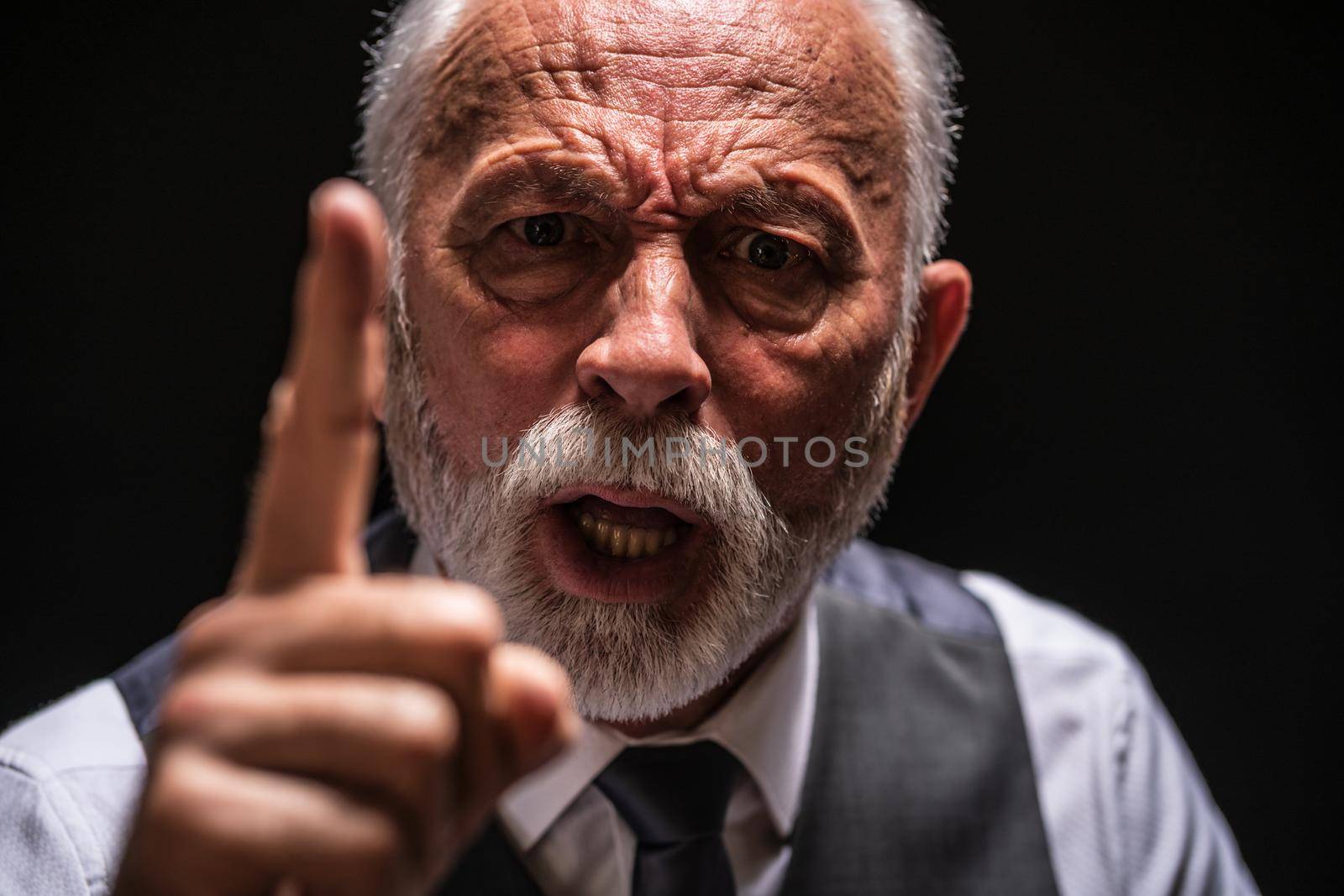 Portrait of angry senior man who threatens. Black background.