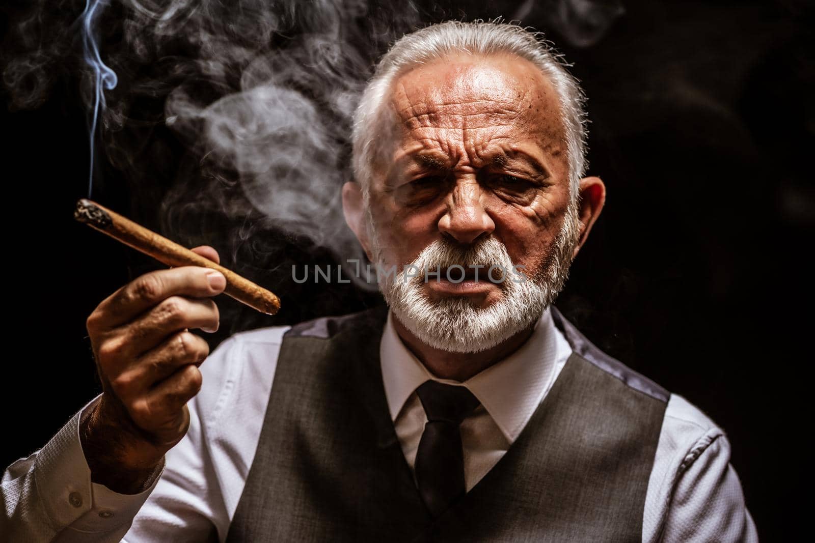 Portrait of serious senior man who is smoking cigar.