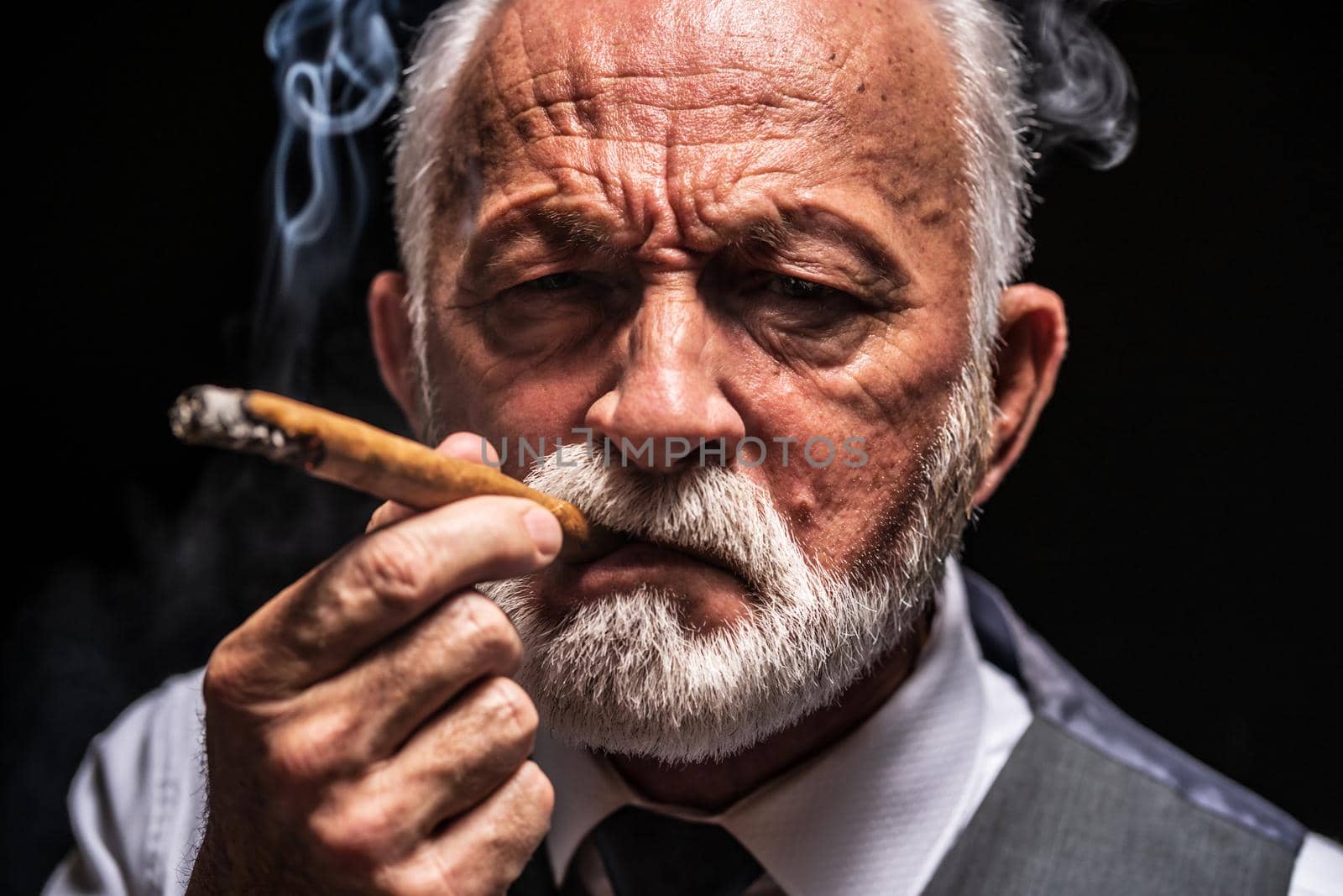 Portrait of serious senior man who is smoking cigar.